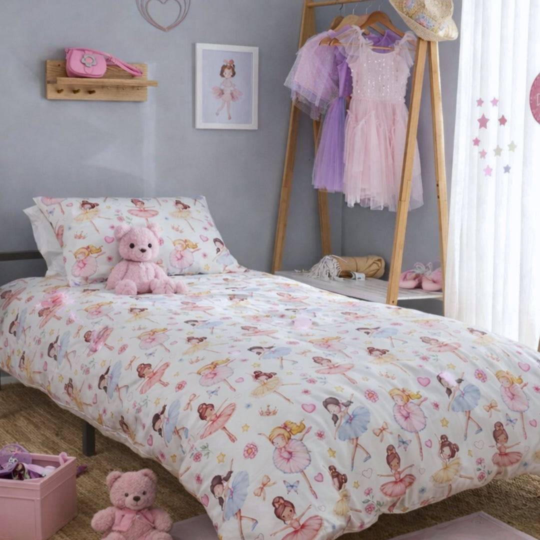 A children's bed dressed in a ballerina themed duvet cover and pillowcase set printed with colourful ballerina illustrations, styled in a bedroom with a wooden floor, pink accessories, and a dress rack.