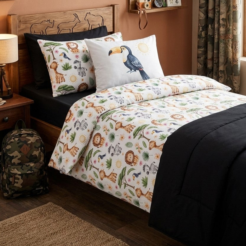 A children's bedding set styled on a bed in a bedroom, featuring a white duvet cover and matching pillowcases with a colorful safari animal print, accented by a black fitted sheet, comforter and a toucan-print accent pillow.