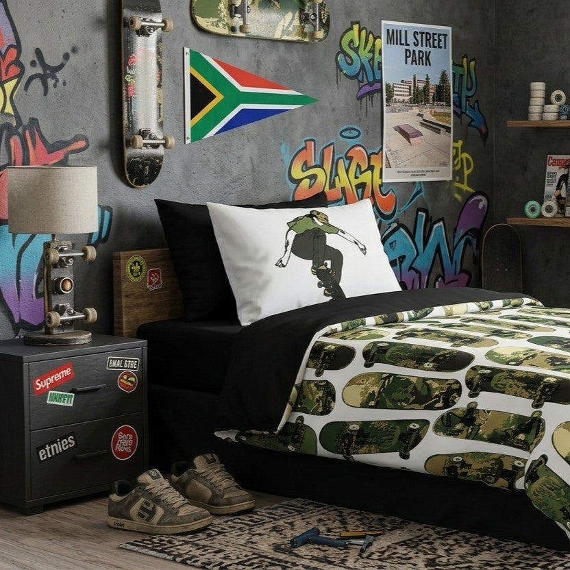 A styled bedroom scene featuring a bed with a white comforter printed with green camouflage skateboards, a black bed frame, a white pillow with a skateboarder graphic, black fitted sheet and top sheet and a dark gray wall decorated with graffiti, skateboards, stickers, and posters.