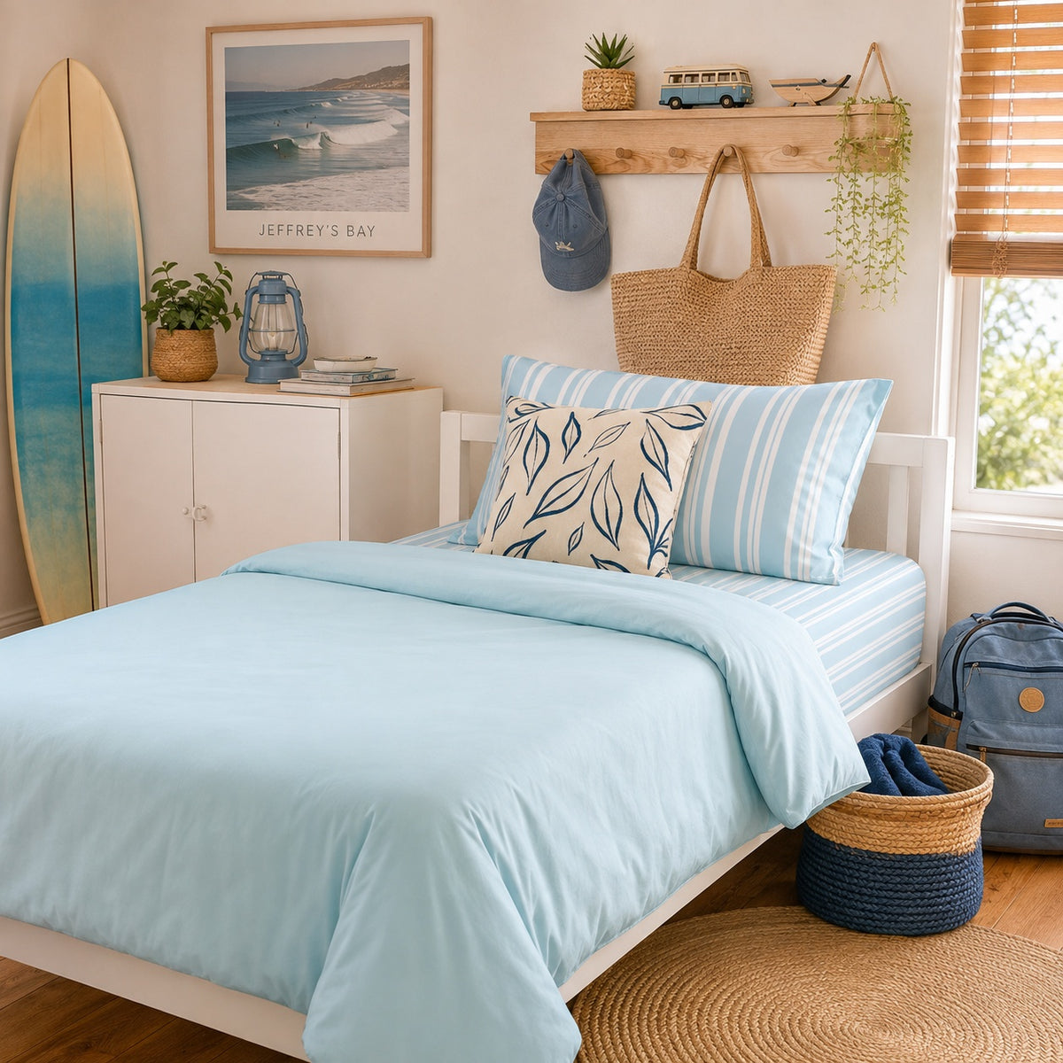 A light blue striped bedding set with a matching striped pillowcase and a decorative leaf-patterned accent pillow, styled on a bed in a bright, coastal-themed bedroom.
