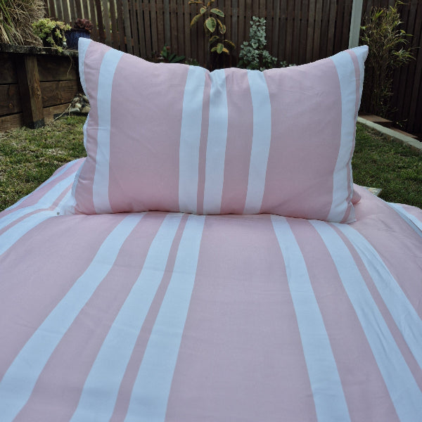Pink and white striped bedding set with a pillow on a bed outdoors.