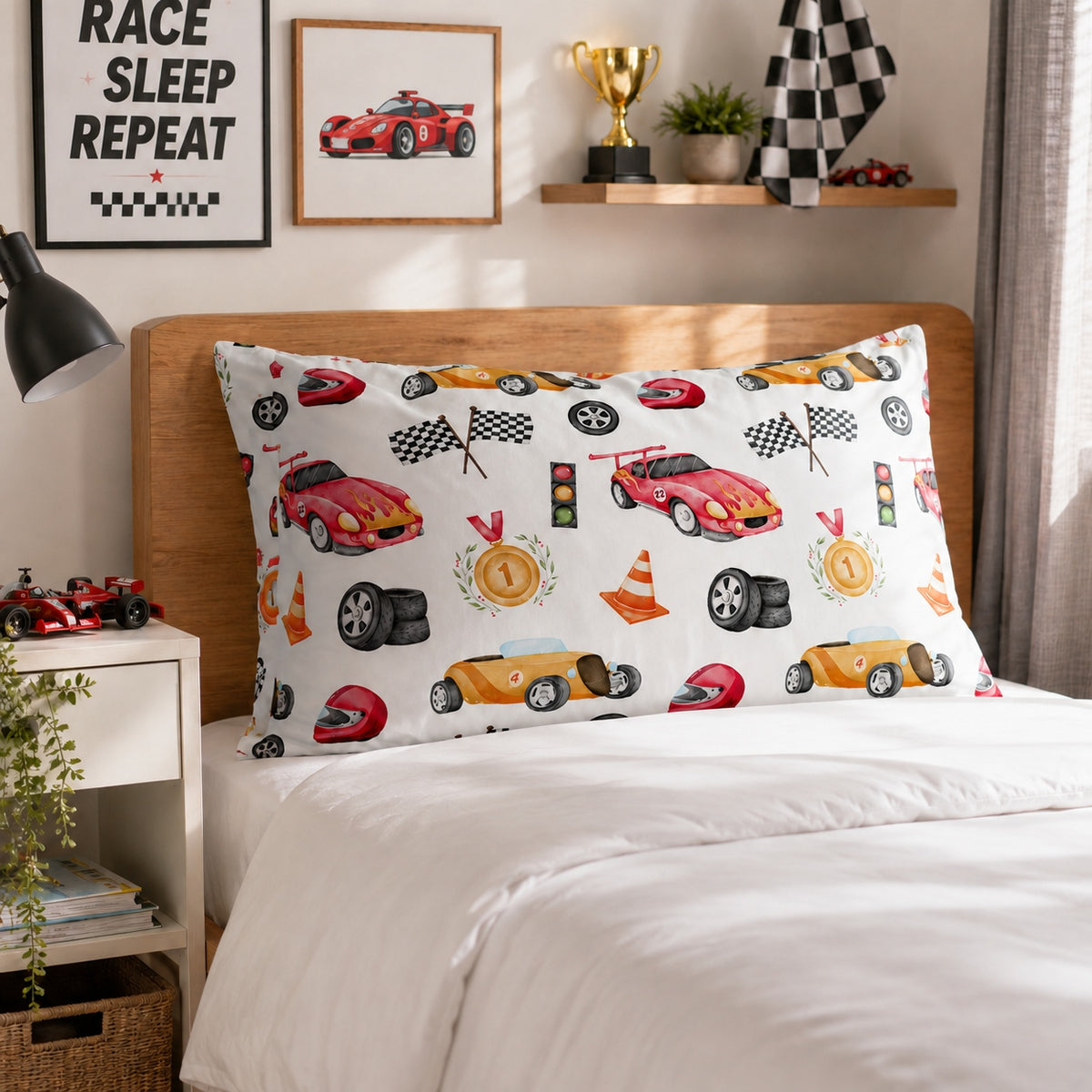 A white racing-themed kids pillowcase with a colorful print of sports cars, checkered flags, helmets, and track elements, displayed on a bed in a styled bedroom setting.