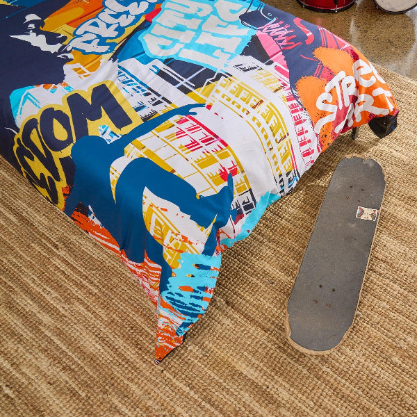 Colorful skateboard deck on carpeted floor with colourful hip hop themed duvet cover corner showing floor