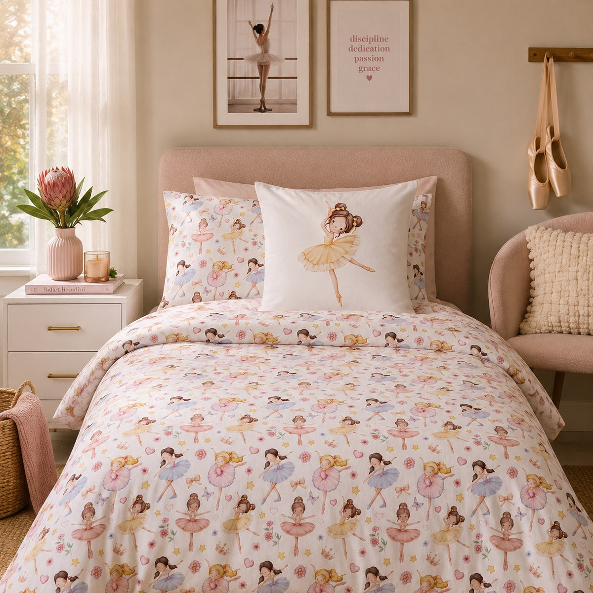 A neatly made bed in a softly styled bedroom featuring a white duvet cover and matching pillowcases printed with ballerina figures in pastel pink, yellow, blue, and green. A central white pillow displays a larger ballerina illustration.