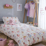A children's bed dressed in a ballerina themed duvet cover and pillowcase set printed with colourful ballerina illustrations, styled in a bedroom with a wooden floor, pink accessories, and a dress rack.