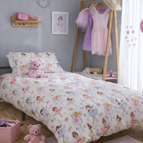 A children's bed dressed in a ballerina themed duvet cover and pillowcase set printed with colourful ballerina illustrations, styled in a bedroom with a wooden floor, pink accessories, and a dress rack.