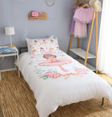 A single bed dressed in a ballerina themed duvet cover and matching pillowcase featuring a watercolour ballerina print with pink roses and pastel illustrations, styled in a bedroom with a side table, lamp, wall shelf, and clothing rack.