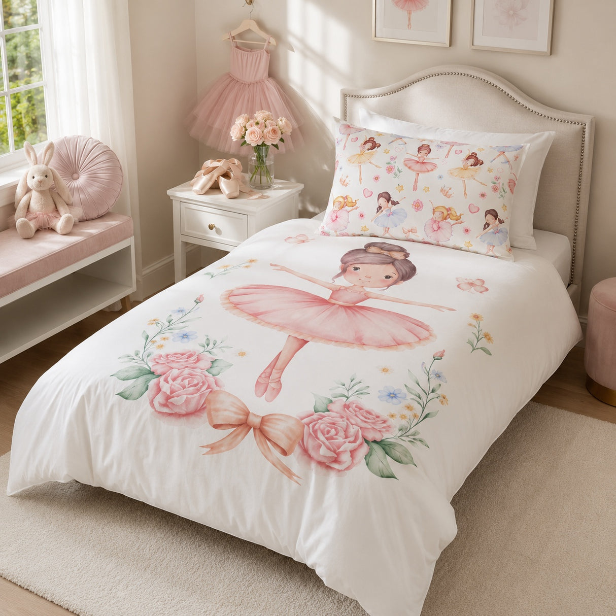 A white single bed dressed in a ballerina-themed kids bedding set, featuring a large pink ballerina print on the duvet and a matching floral pillow. The bed is styled in a soft pink children's bedroom with a nightstand, bunny plush, and framed wall art.