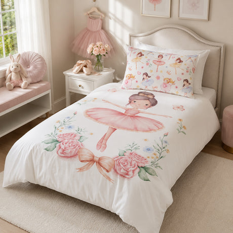 A white single bed dressed in a ballerina-themed kids bedding set, featuring a large pink ballerina print on the duvet and a matching floral pillow. The bed is styled in a soft pink children's bedroom with a nightstand, bunny plush, and framed wall art.