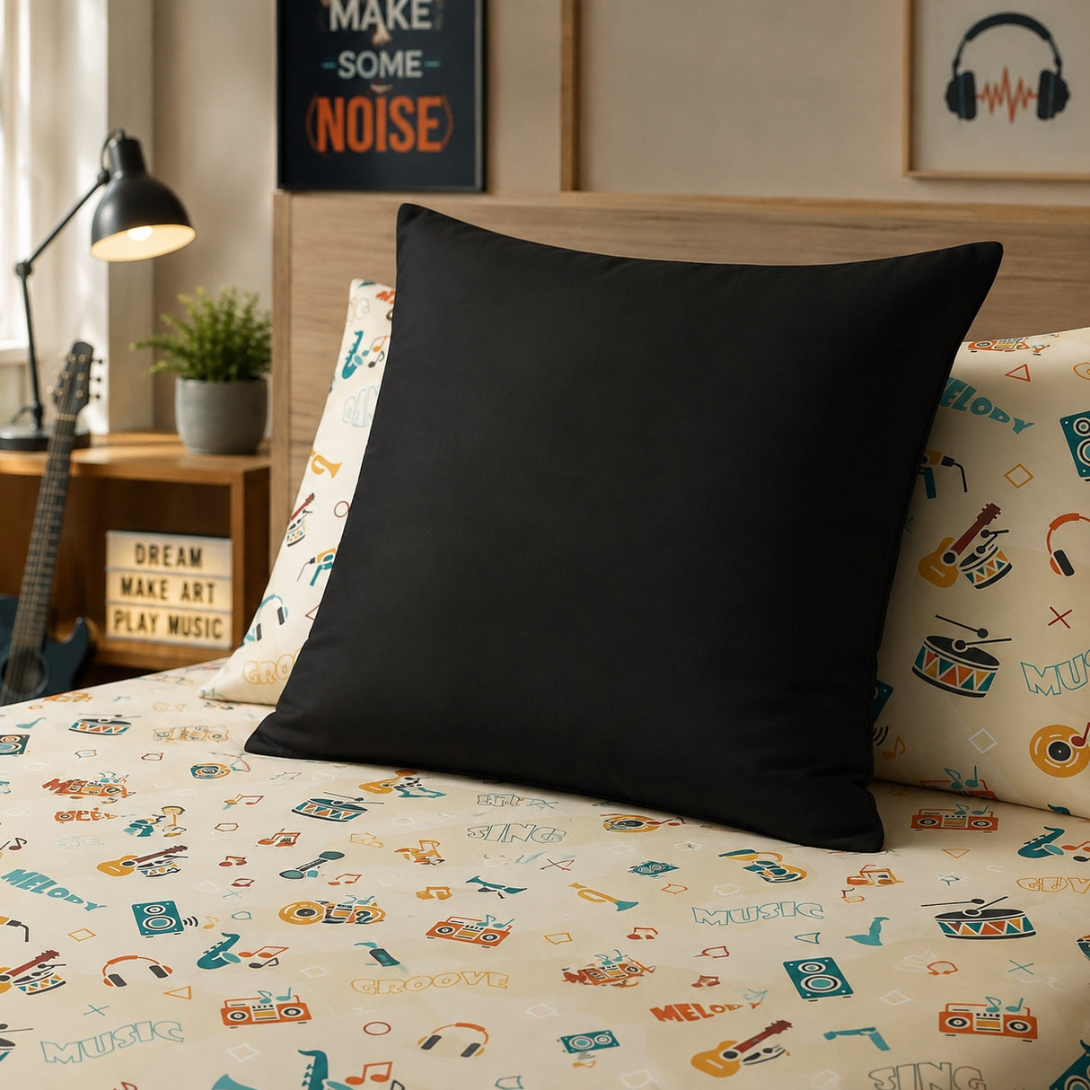 A solid black continental pillow displayed on a bed with a beige and multicolor music-themed patterned sheet and matching pillowcases, set in a cozy bedroom environment.