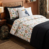 A children's bedding set styled on a bed in a bedroom, featuring a white duvet cover and matching pillowcases with a colorful safari animal print, accented by a black fitted sheet, comforter and a toucan-print accent pillow.