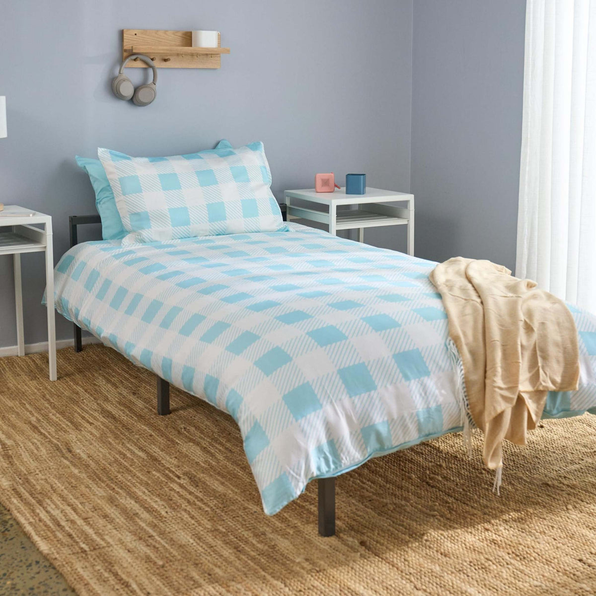 Bed with reversible blue gingham check bedding in a room with gray walls and wooden flooring. 