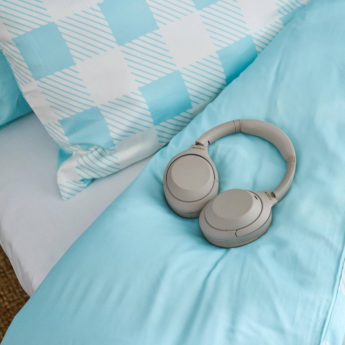 Gray headphones on a light blue bedspread with check blue and white pillows in the background.  Jo's Dreamland family designed organic kids bedding South Africa
