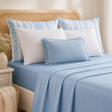 A neatly made bed with light blue bedding, including a fitted sheet, duvet, and matching pillows, styled with white and blue striped pillows in a bright bedroom setting.