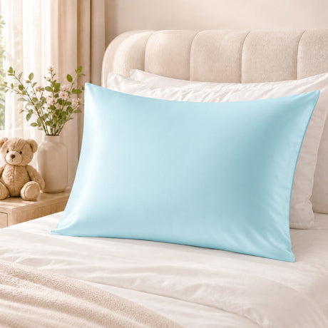 A light blue pillowcase displayed on a bed with white bedding, a beige tufted headboard, and a small teddy bear next to a vase of flowers.
