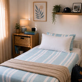 Image of a bedroom styled with a blue striped bamboo bedding set with white fitted sheet and white pillow. 