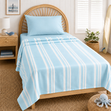 A light blue bedding set with white vertical stripes, including a top sheet and matching pillow, styled on a wooden bed in a bright, nautical-themed bedroom.
