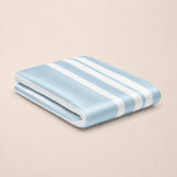 A folded light blue bamboo top sheet with white stripes, displayed on a solid beige background.