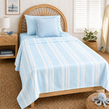 A light blue bedding set with white vertical stripes, including a top sheet and matching pillowcases, styled on a wooden bed in a bright, beach-themed bedroom.