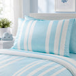 Light blue and white striped bedding set with matching pillowcases on a bed, styled in a bright, airy bedroom with a small cloud-shaped pillow on the bedside table.