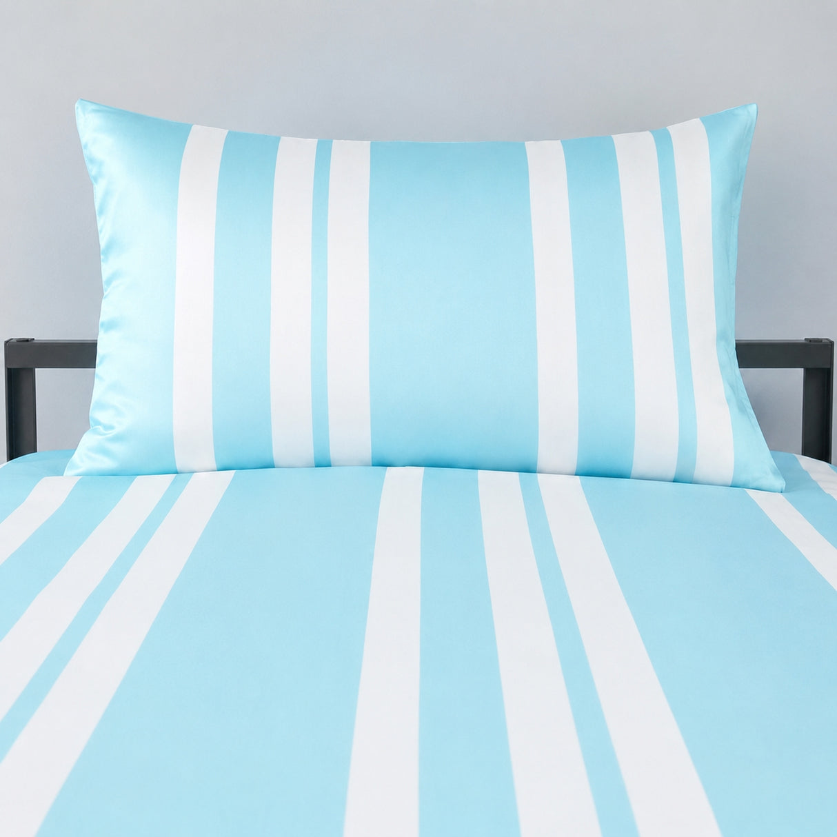 A light blue and white striped bedding set featuring a matching pillowcase and sheet on a bed frame, shown against a neutral gray wall.
