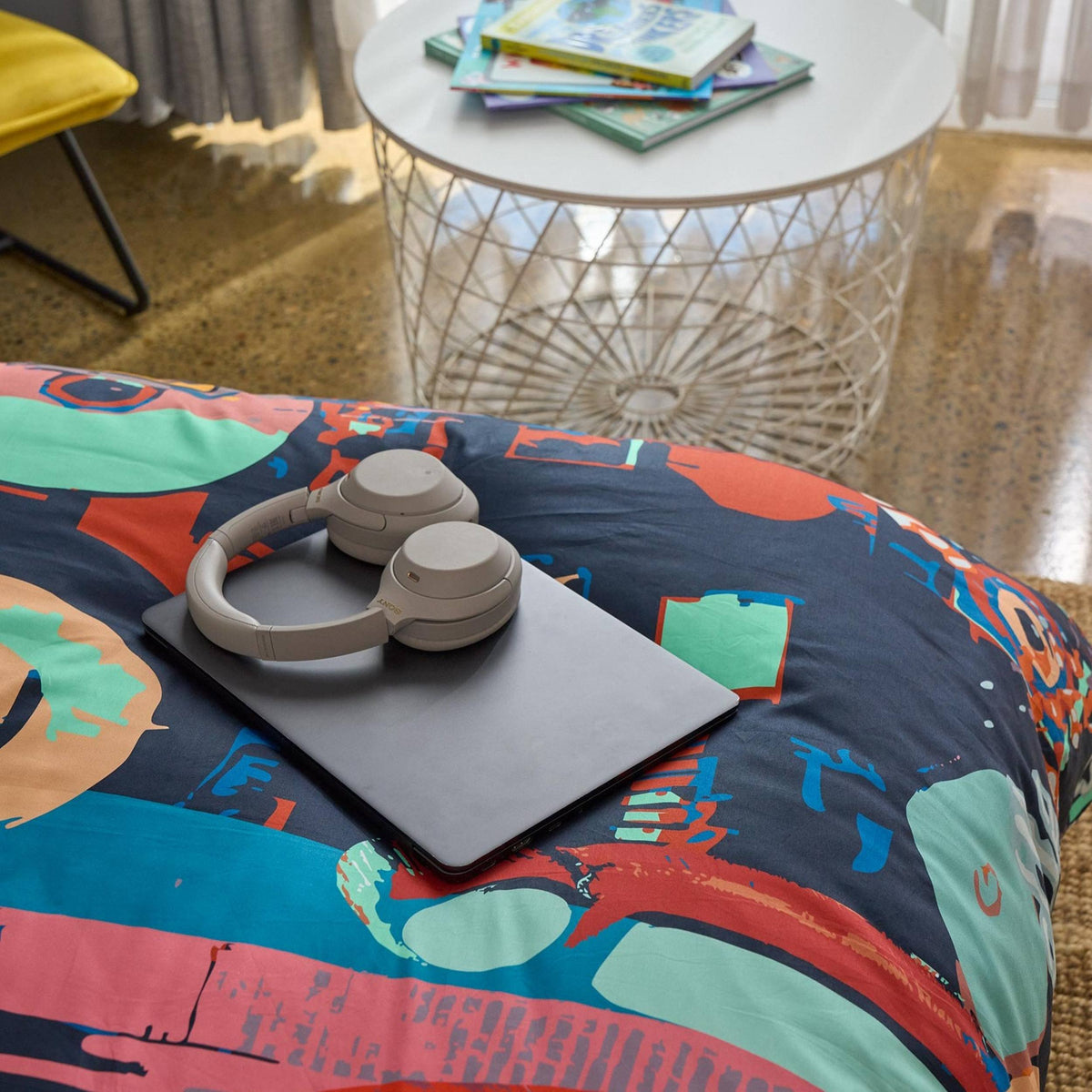 Colorful bedspread with a laptop and headphones on a table in the background
