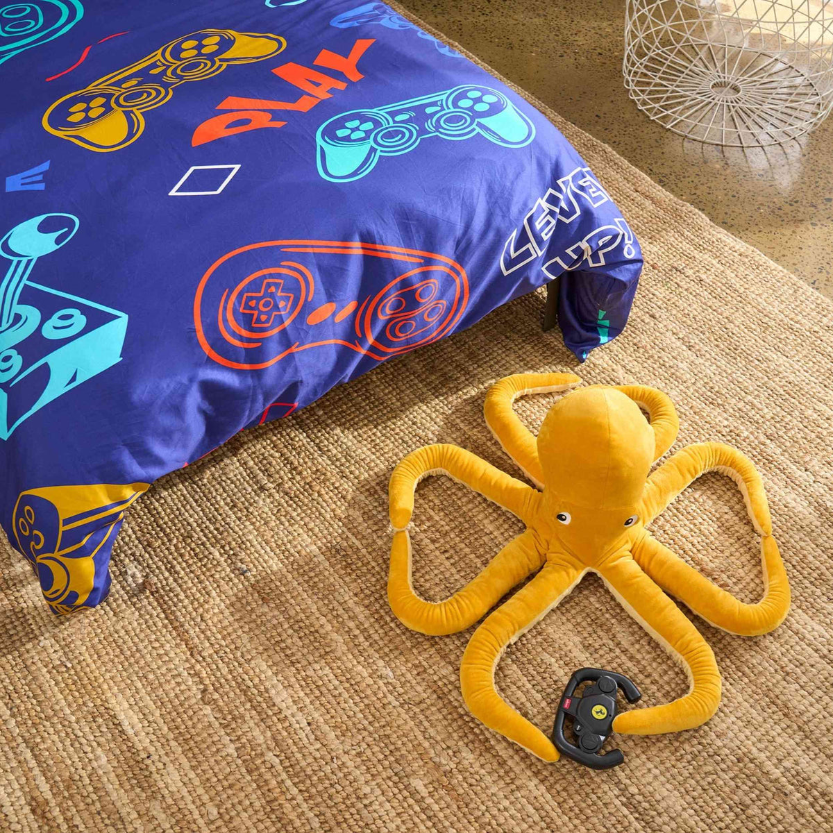 Yellow octopus-shaped toy with game controller attachment on a carpeted floor next to a colorful gaming-themed duvet cover set.
