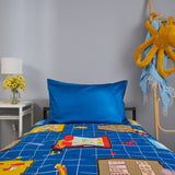 Bed with blue maths themed bedding featuring cartoon designs, next to a white nightstand with a lamp and flowers.