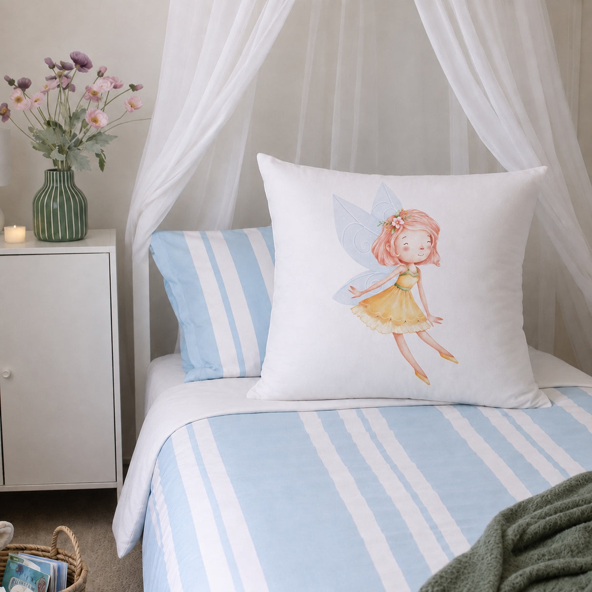 A white decorative continental pillow featuring a watercolor illustration of a fairy in a yellow dress, styled on a bed with light blue and white striped bedding and a matching pillow in a bedroom setting.