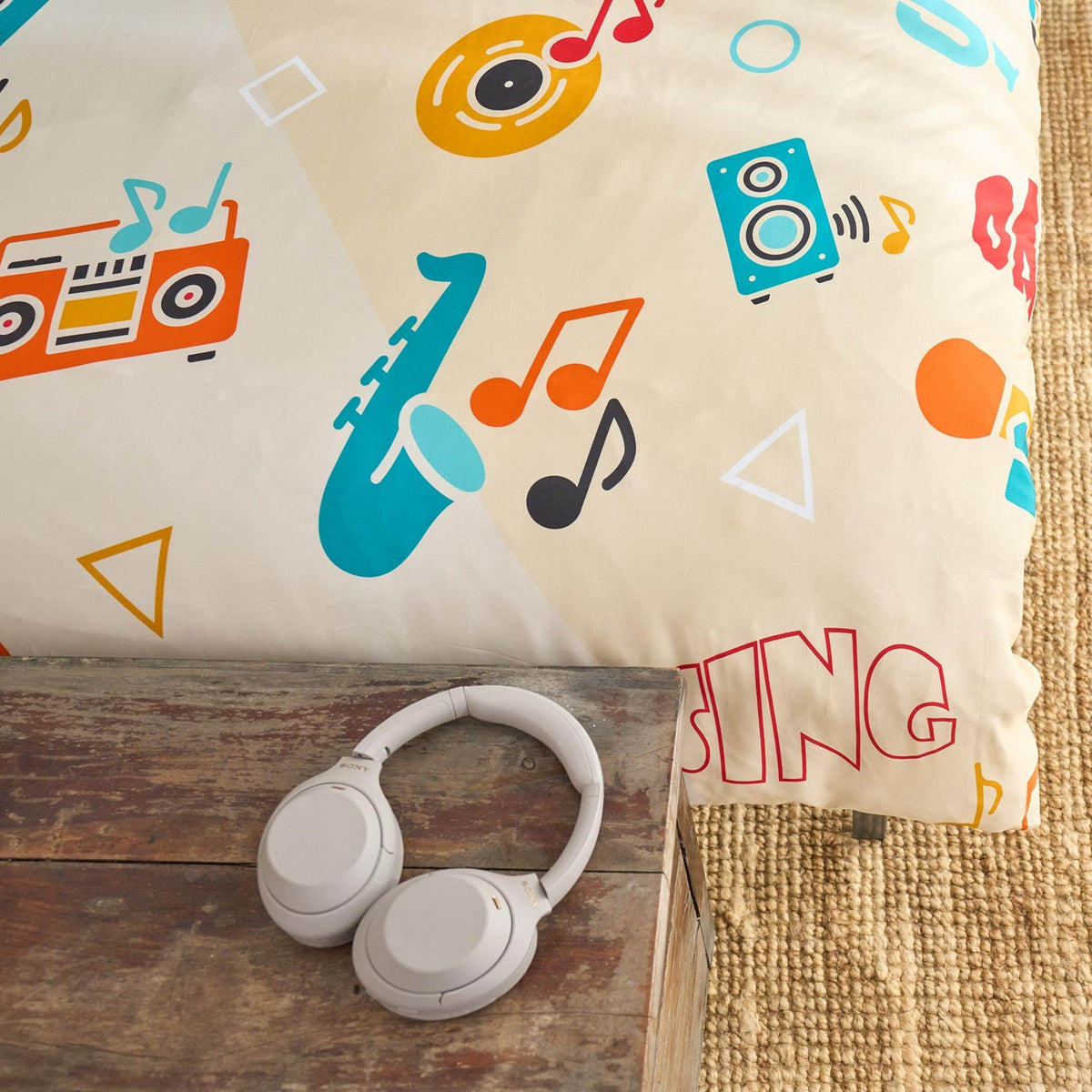 Music-themed duvet cover with colorful designs and 'SING' text, next to a pair of white headphones on a wooden surface.