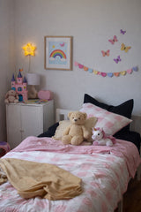 Children's bedroom with pink and white check bedding, toys, and decorative elements.