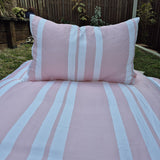 Pink and white striped bedding set with a pillow on a bed outdoors.