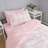 Pink and white checkered bedding set on a single bed, featuring a solid pink sheet and pillowcase with a patterned duvet cover, styled in a bedroom setting next to a white bedside table.