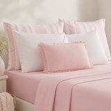 Pink bedding set on a bed with a solid pink sheet, white pillows, and striped pink-and-white pillows, styled in a soft bedroom setting.