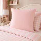 A pink bedding set styled on a bed, featuring a solid light pink continental pillowcase, a pink and white gingham accent pillow, and a pink and white striped duvet cover, set in a soft pink bedroom.