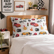 A white racing-themed kids pillowcase with a colorful print of sports cars, checkered flags, helmets, and track elements, displayed on a bed in a styled bedroom setting.