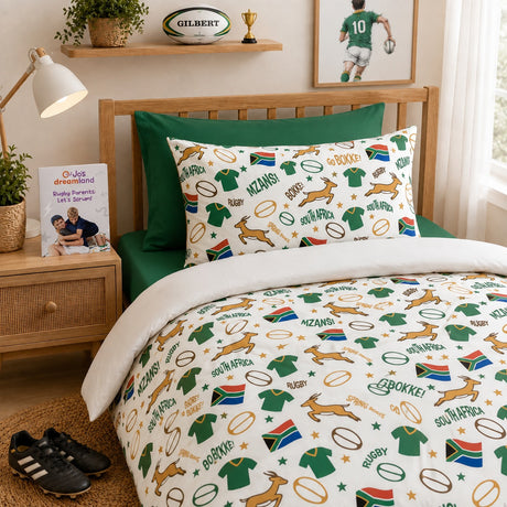 A bed dressed in a South Africa rugby-themed kids bedding set, featuring a white duvet cover and matching pillowcase printed with green jerseys, rugby balls, Springboks, and rugby scores, styled in a warm bedroom setting.