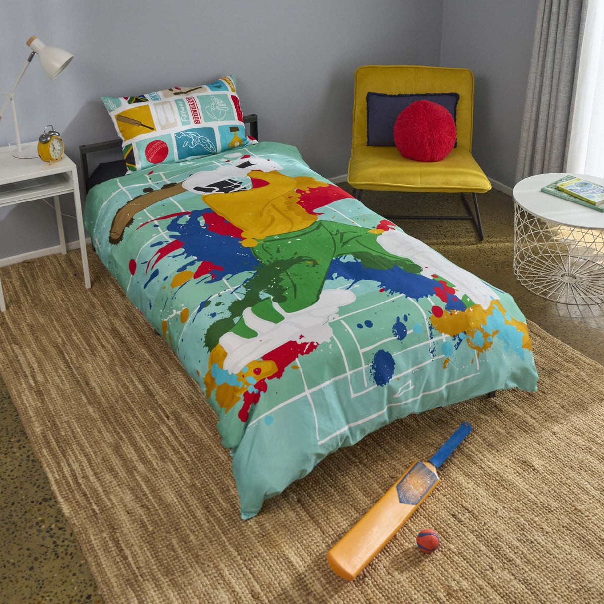A colorful South African Cricket themed bedding set on a single bed in a modern bedroom. The duvet cover features a green batter  graphic over a light teal background with paint splatters in red, yellow, blue, and white.