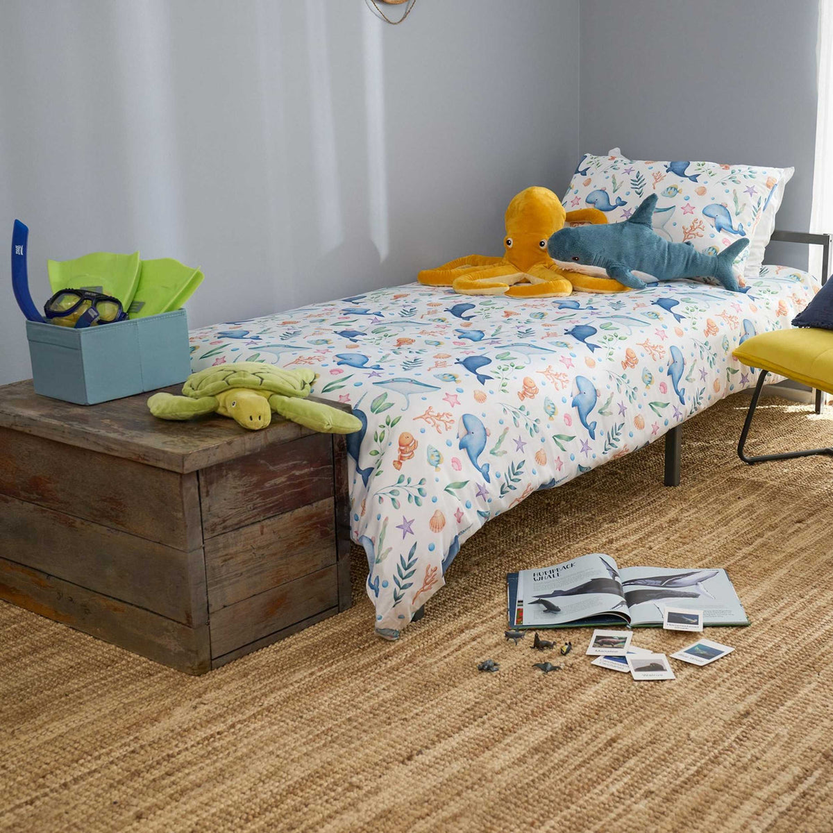 Children's bedroom with a bed featuring a colorful sea animals themed kids bedding set, toys, and books on a wooden bench.