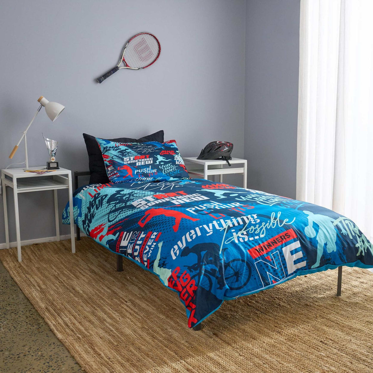 Bedroom with blue and red sports themed bedding set on a bed, tennis racket and helmet on shelves.
