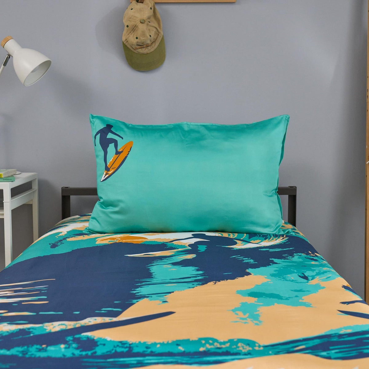 Teal pillowcase with a surf design on a bed with matching bedding in a room.