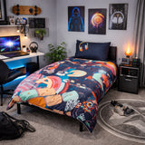 Room interior with a bed featuring a colorful technology themed duvet cover, desk with laptop, and wall art.