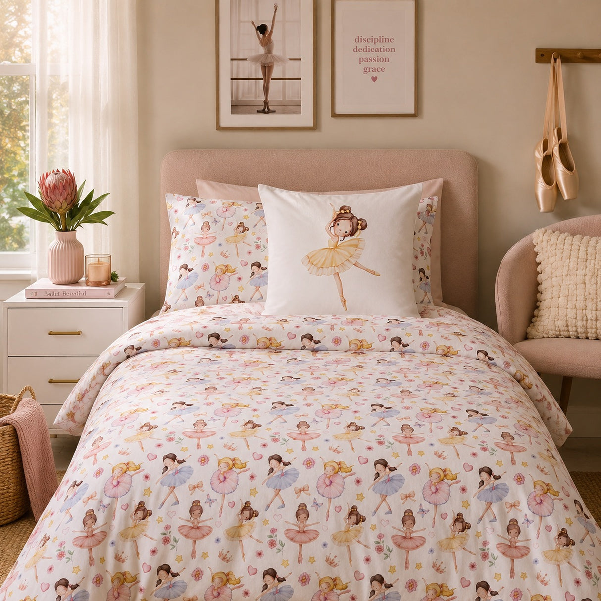 A neatly made bed in a softly styled bedroom featuring a white duvet cover and matching pillowcases printed with ballerina figures in pastel pink, yellow, blue, and green. A central white pillow displays a larger ballerina illustration.