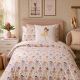 A neatly made bed in a softly styled bedroom featuring a white duvet cover and matching pillowcases printed with ballerina figures in pastel pink, yellow, blue, and green. A central white pillow displays a larger ballerina illustration.